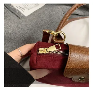 Detail of burgundy suede handbag with brown leather handle and gold metal hardware