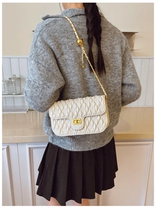 Detail of white quilted crossbody bag featuring golden ball adjustment and leather chain