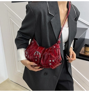 Detail of dark red croc-embossed underarm bag with silver buckles and metal rivets