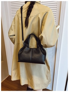 Detailed view of black lychee grain leather dumpling bag worn on a beige trench coat
