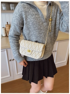 Detail of white quilted handbag with golden chain strap worn in a cozy indoor setting