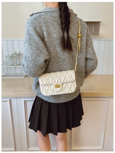 Detail of white quilted crossbody bag with gold chain strap worn by a model