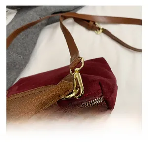 Close-up of burgundy suede bag featuring a leather strap with gold-tone metal hook detail