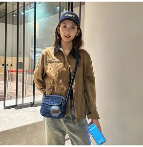 Close-up of a blue washed denim crossbody bag with a brown leather patch on a model