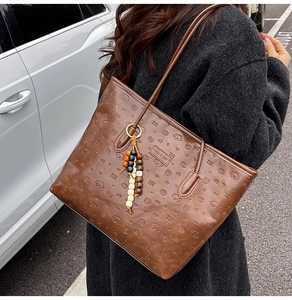 Macro shot of brown leather tote bag showing embossed cartoon dog patterns and bead charms