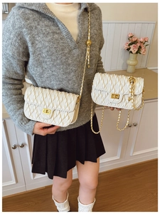 Detail of white quilted handbag with adjustable gold ball chain strap and turn-lock