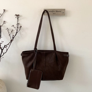Detail of a dark brown large tote bag featuring a matching small pouch on a minimalist wall