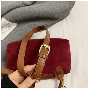 Close-up of burgundy velvet bag with brown leather strap and golden metal buckle details