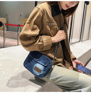 Detailed view of vintage washed denim crossbody bag with brown leather brand patch
