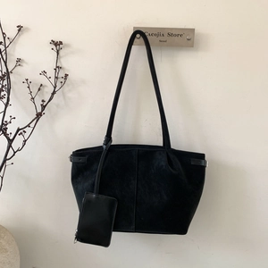 Detail of black tote bag with side buckle and matching small zipper pouch hanging on hook