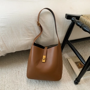 Detail of brown leather bucket bag featuring gold rotating lock and adjustable strap