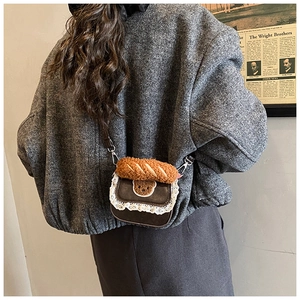 Detail of mini leather crossbody bag with lace trim, bear patch, and plush baguette handle