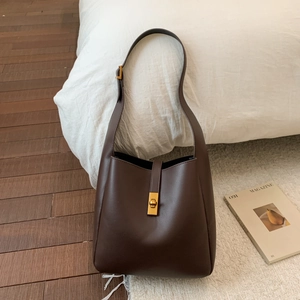 Detail of dark brown leather bucket bag with gold clasp on a cozy plush carpet