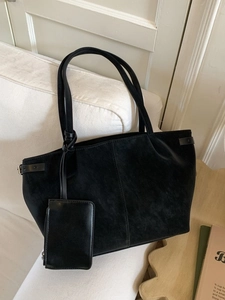 Large black matte leather tote bag with a small coin purse on a soft white sofa