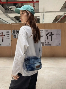 Street style view of a washed blue denim crossbody bag with vintage aesthetic and leather patch