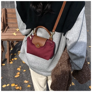 Detail of burgundy nylon mini bag with leather flap and handle against an autumn background