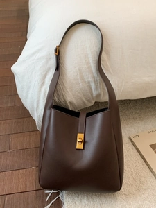 Minimalist deep coffee leather bucket bag with gold metal lock on white bedding