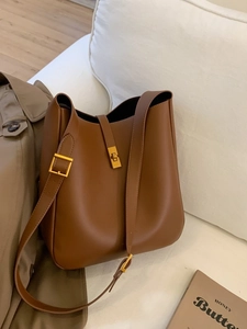 Brown leather bucket bag with gold twist lock and adjustable strap on neutral background