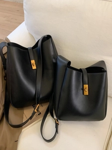 Chic black leather bucket bag with gold clasp shown in large and small sizes on a sofa