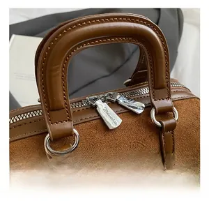Detailed close-up of brown suede Boston bag featuring silver hardware and dual zippers