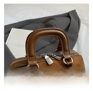 Close-up of brown suede handbag featuring smooth leather handles and silver dual zippers