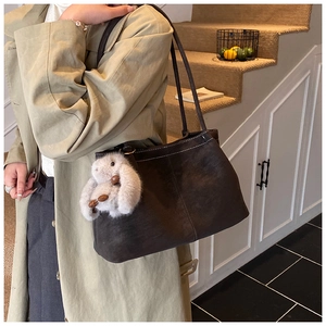 Detail of dark brown tote bag with contrast stitching and rabbit plush charm on a strap
