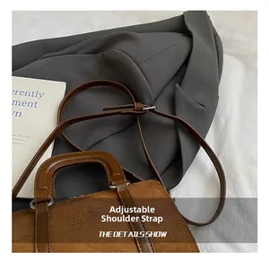Close-up of brown suede handbag with adjustable strap and dual handles next to a blazer