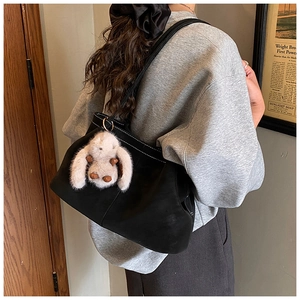 Detail einer schwarzen Leder-Shopper-Tasche mit weißem Hasenanhänger am Modell getragen