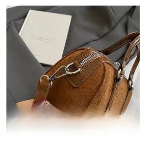 Detail of dark brown suede handbag featuring metal hooks and smooth zipper closure