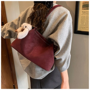 Detail of burgundy tote bag with white stitching and cute rabbit charm on a model