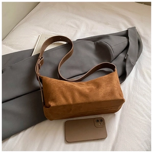Sac bandoulière en suédine marron sur lit blanc avec un blazer chic et des livres