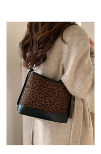 Detailed view of leopard print suede shoulder bag with black leather trim on beige coat