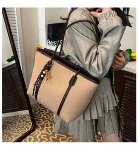 Detail view of large tote bag featuring beige PU leather patchwork and striped tassel charm