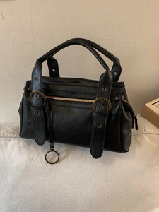 Sac Boston en cuir noir rétro avec ferrures métalliques et breloques vintage en nature morte