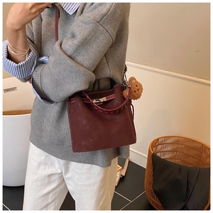 Detail of burgundy leather bucket bag with woven handle, metal lock, and plush bear charm