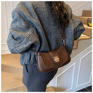 Detail of a brown suede and leather crossbody bag featuring a round gold metal buckle