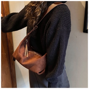 Détail d'un sac bandoulière en daim marron avec franges porté sur un pull d'automne