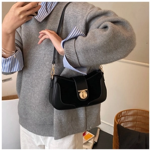 Close-up of black leather underarm bag with gold twist lock on a model outfit
