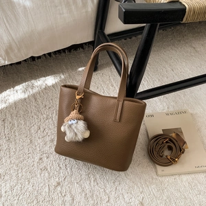 Detail of dark brown lychee leather tote bag with a grey plush charm and shoulder strap