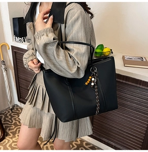 Detail of black leather tote bag with stylish bead tassel charm and vertical stitching