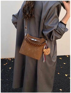 Detail view of brown suede bucket bag featuring woven handle and cute plush bear charm