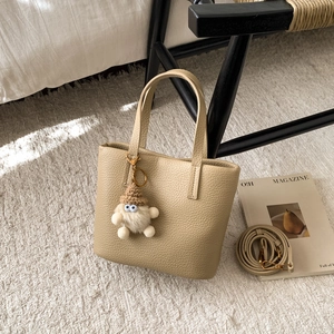 Detail of beige lychee grain leather handbag with cute plush monster charm on a carpet