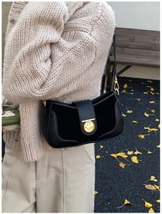 Close-up of a black minimalist underarm bag with an oval gold buckle on a beige knit sweater