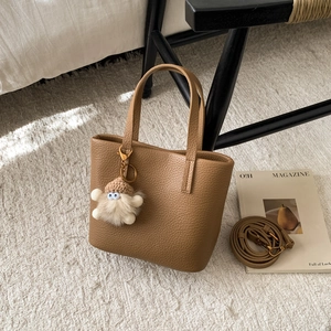 Close-up of brown litchi pattern leather tote bag with cute plush doll charm on rug