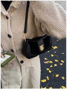 Detail of black leather baguette bag with gold twist lock and adjustable metal buckle strap