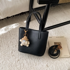 Detail of black pebbled leather tote bag with a cute plush monster charm and strap