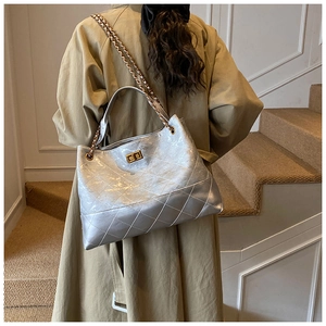Detail view of large silver quilted tote bag with metal chain strap on a trench coat