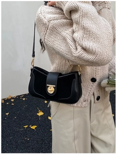 Chic black leather underarm bag with gold metal clasp on a model in an outdoor setting