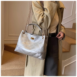 Detail of silver quilted tote bag featuring gold chain strap and metallic lock clasp
