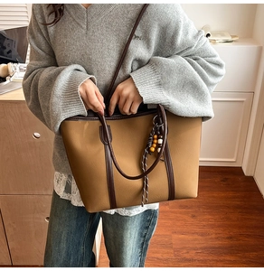 Detail view of large brown tote bag featuring contrast straps and decorative beaded tassel